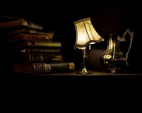 turned on desk lamp beside pile of books