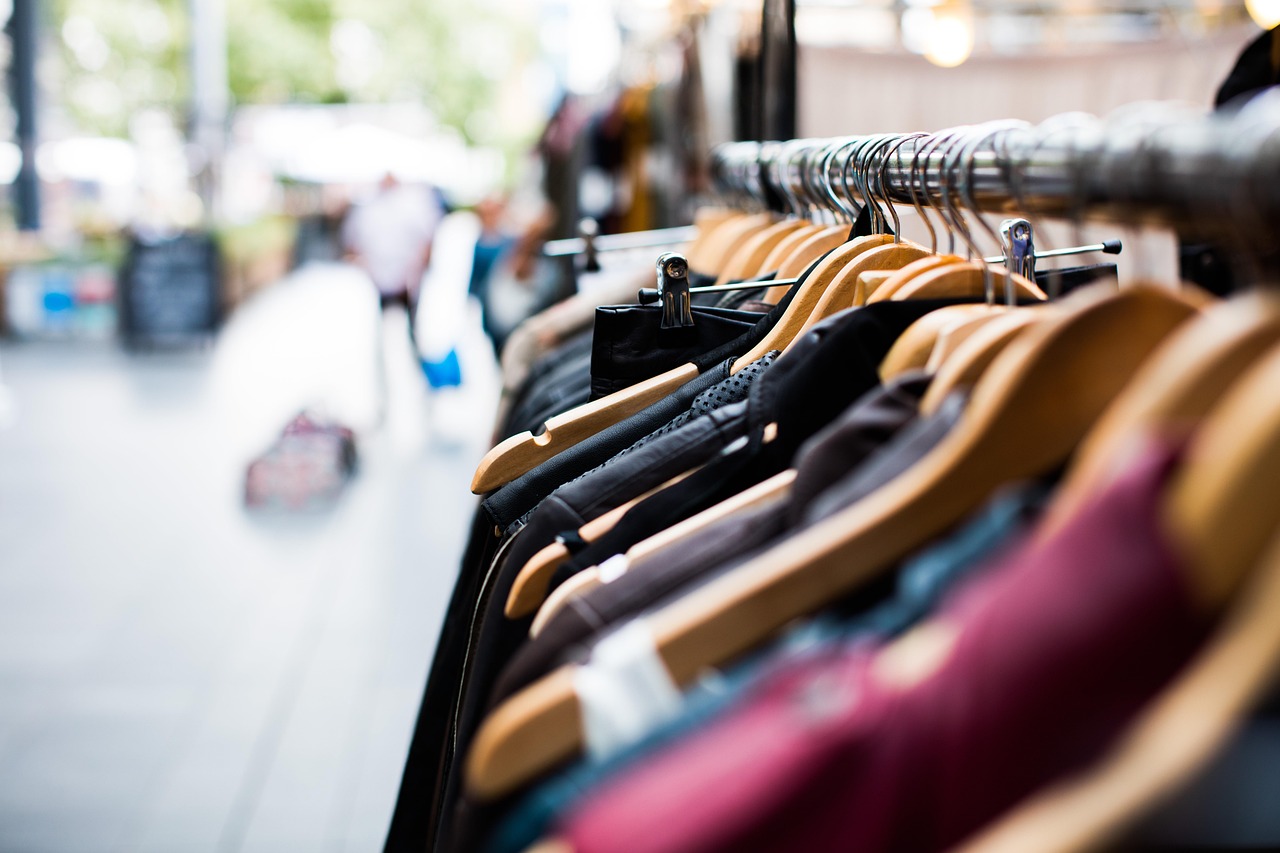 Kleurrijke vintage kleding hangend aan een rek in een kringloopwinkel